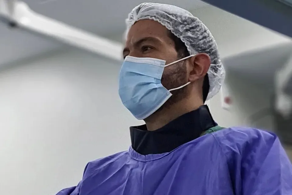 Dr. Luciano Morais de touca, máscara e avental azul durante um procedimento