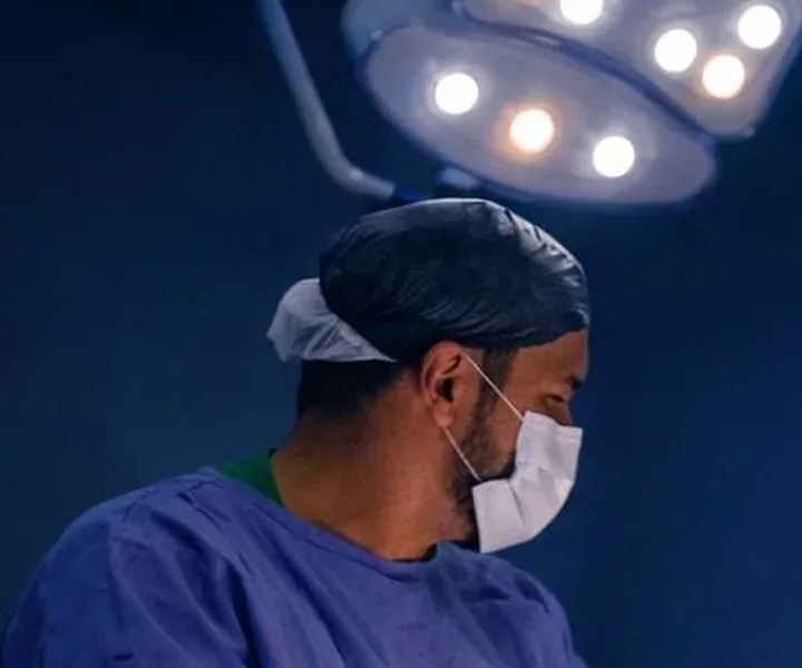Dr. Luciano Morais operando sob o foco de luz, de avental azul